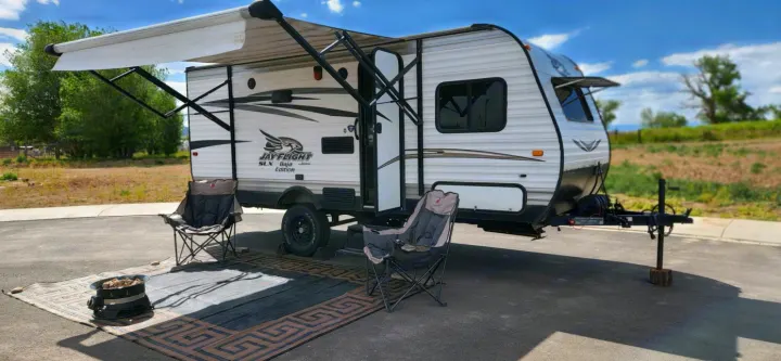 This RV rental shows a white travel trailer with an extended awning, two camping chairs, a mat, and a fire pit set up outside.. Jayco Jay Flight SLX 2016