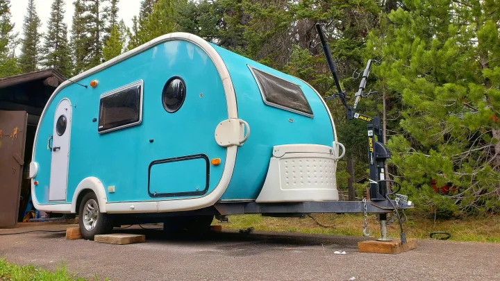 Vibrant teal teardrop RV rental with a bike rack, parked in a wooded area. Perfect for your next camping adventure.. Dutchmen T@da 2009