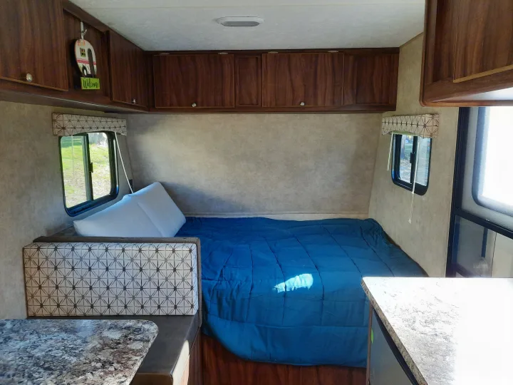 Inside a cozy RV rental, featuring a bed with blue bedding, patterned seating, and wood cabinets. Ready for your next camping trip!. Forest River Viking Saga 2016