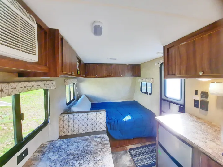 This **rv rental** interior features a bright space with a cozy bed, a dinette, a small kitchen, and an AC unit.. Forest River Viking Saga 2016