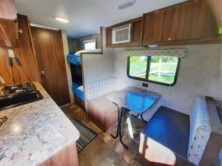 Interior of an RV rental showing a kitchen, dinette with table, and bunk beds. A compact and functional camper living space.. Forest River Viking Saga 2016