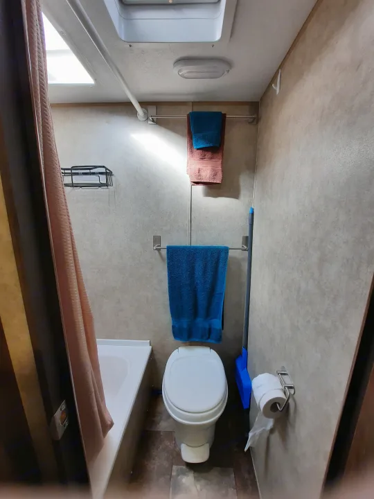 An RV rental bathroom setup, showing a white toilet, small tub/shower with peach curtain, and blue/rust towels.. Forest River Viking Saga 2016