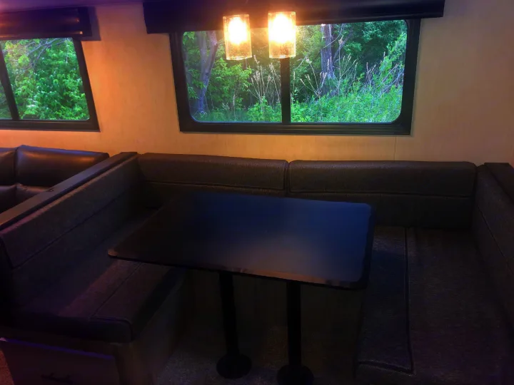 Spacious RV rental interior with a cozy dinette seating area, black table, and large windows showing lush greenery. Perfect for your next adventure.. Forest River Cherokee Alpha Wolf 2022