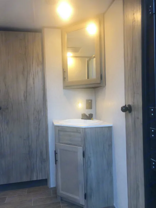 Compact RV rental bathroom features a wood-look vanity, sink, and mirror, designed for efficient travel.. Forest River Cherokee Alpha Wolf 2022
