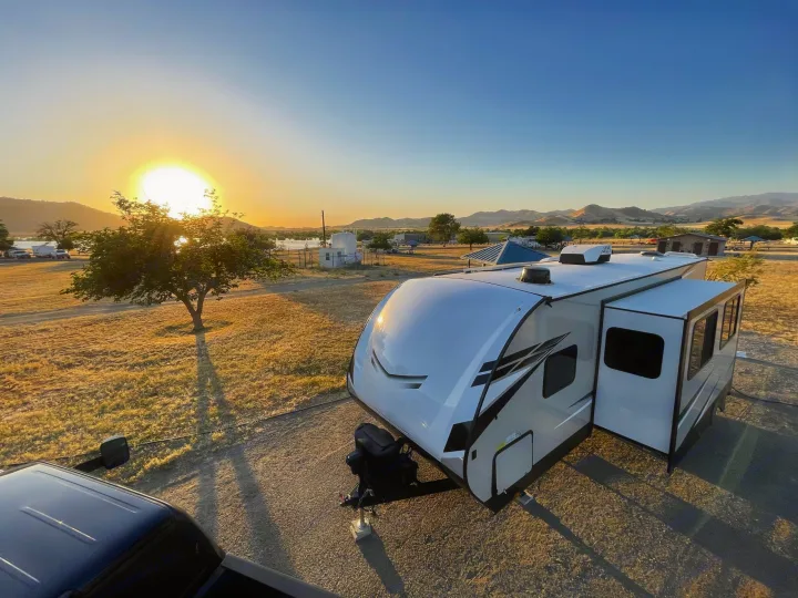 A white RV rental travel trailer parked at a scenic lakeside campground during golden hour, with hills in the background.. Starcraft Super Lite 2022