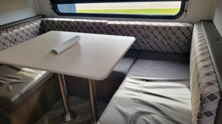 RV rental interior: Light dining table with grey vinyl and patterned fabric booth seating. Window visible.. Forest River EVO 2021