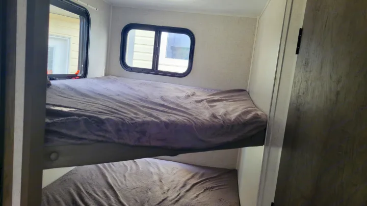 Inside an RV rental, comfortable bunk beds with soft blankets and two windows letting in natural light.. Forest River EVO 2021