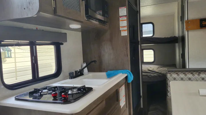 Cozy RV rental interior: kitchen with stove & sink, plus comfortable bunk beds and dinette seating area.. Forest River EVO 2021