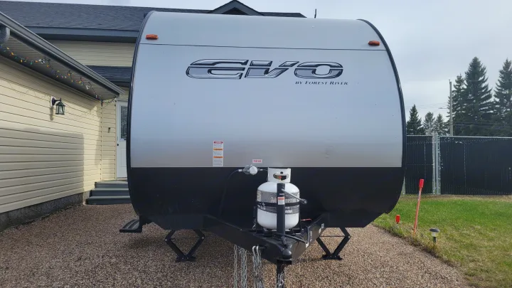 Front of an EVO travel trailer, ready for your next RV rental. Propane tank visible, parked at a home.. Forest River EVO 2021