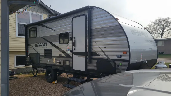 An RV rental, an EVO by Forest River travel trailer, parked in a residential gravel driveway, ready for adventure.. Forest River EVO 2021