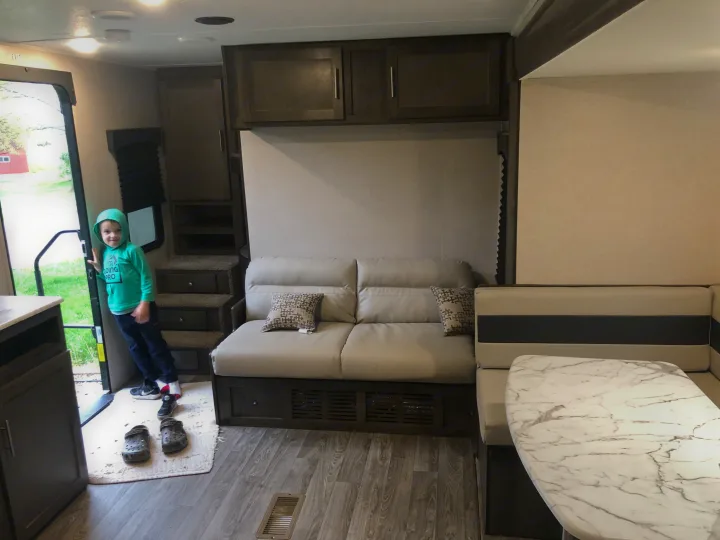 RV rental interior: Child by the doorway, with a sofa, dinette, overhead cabinets, and wood-look laminate floor.. Coachmen Clipper 26BHS 2021