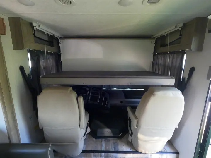 Inside an RV rental: Front cockpit with driver/passenger seats and a cozy overhead bunk. Ideal for road trips and extra sleepers.. Coachmen Pursuit 2021