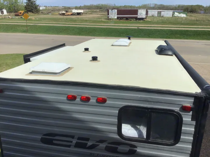 View from above an RV rental: white roof, vents, and awning. Rear of camper with gray siding, window, and red lights.. Forest River EVO 2021