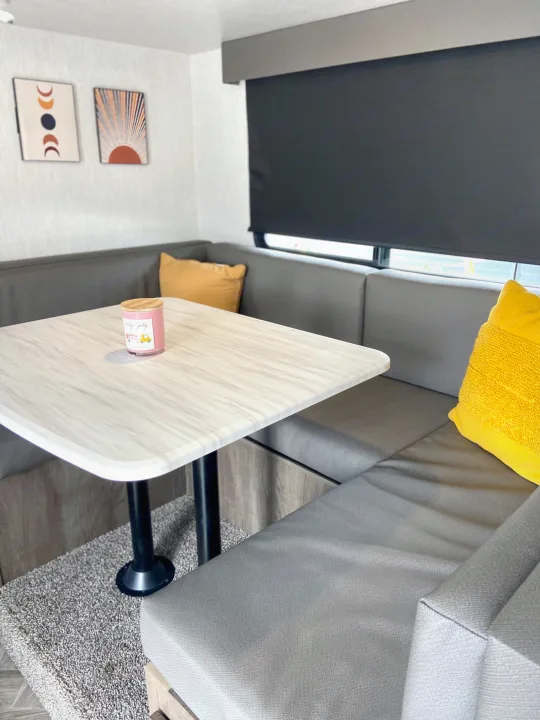 Cozy RV rental dinette with grey seating, a marbled table, and sunny yellow pillows. Modern travel comfort awaits.. Forest River Salem Hemisphere 2022