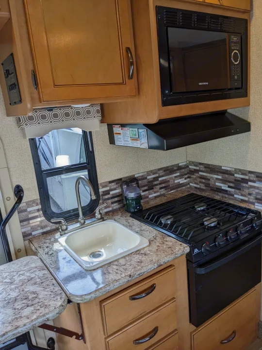 Explore this RV rental's well-equipped kitchen: stove, microwave, sink, and backsplash. Perfect for road trips.. Thor Motor Coach Four Winds 2017