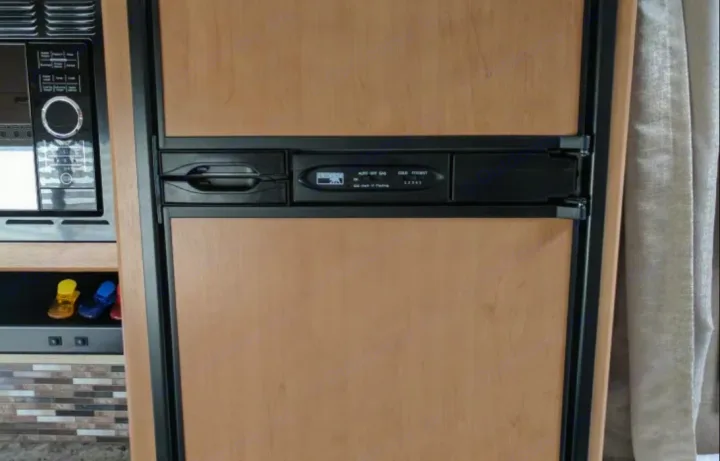 Inside this RV rental, a compact light wood refrigerator/freezer with control panel sits beside a built-in microwave.. Thor Motor Coach Four Winds 2017
