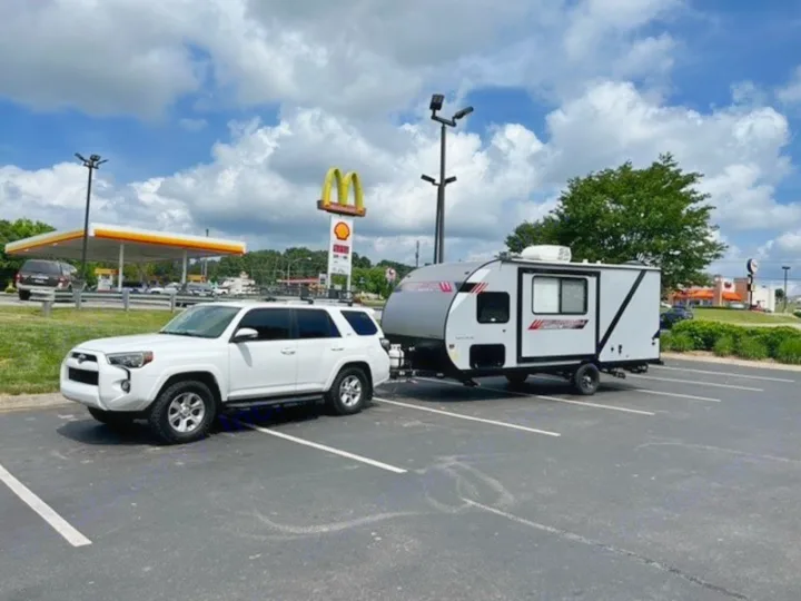 White SUV towing a compact rv rental travel trailer, parked at a gas station.. Forest River Wildwood FSX Platinum 2021