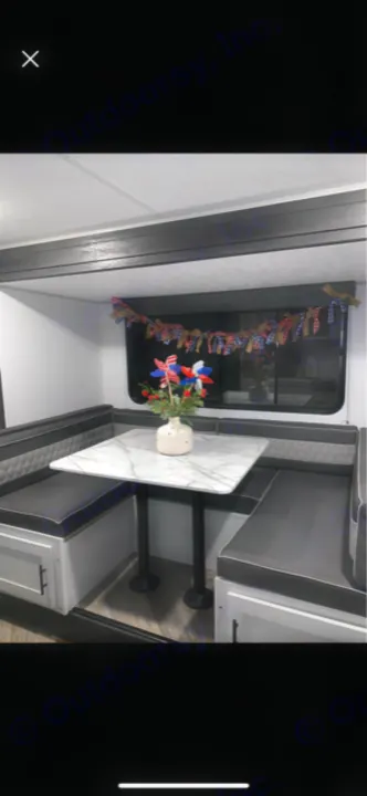 RV rental dinette: Modern U-shaped seating, marble-look table, and patriotic decor. Perfect for comfortable travel.. Forest River Wildwood FSX Platinum 2021