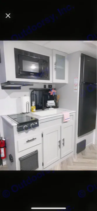 Modern RV rental kitchen features a microwave, two-burner cooktop, sink, and black refrigerator with light gray cabinetry.. Forest River Wildwood FSX Platinum 2021