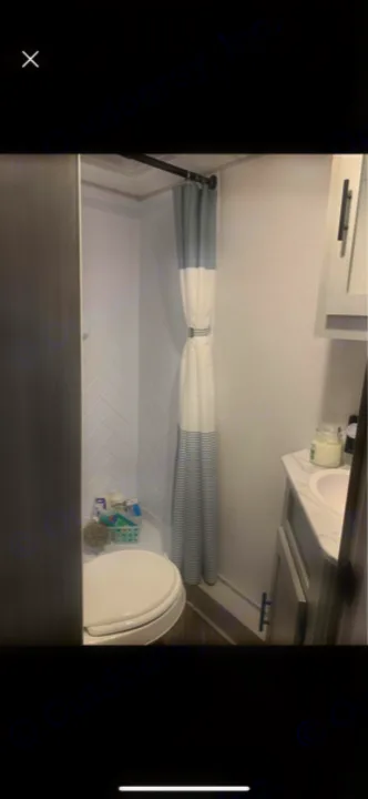 This compact RV rental bathroom features a shower (gray/white striped curtain), toilet, and vanity. Perfect for travel.. Forest River Wildwood FSX Platinum 2021