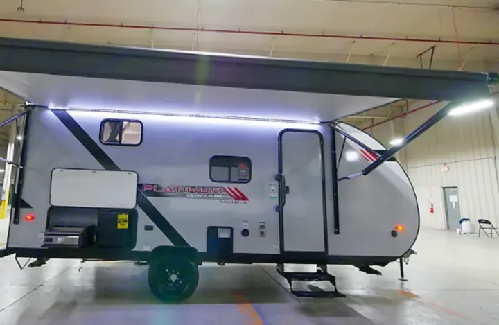 Light gray travel trailer, ideal for rv rental, with an extended awning, bright LED lights, and an outdoor kitchen setup.. Forest River Wildwood FSX Platinum 2021