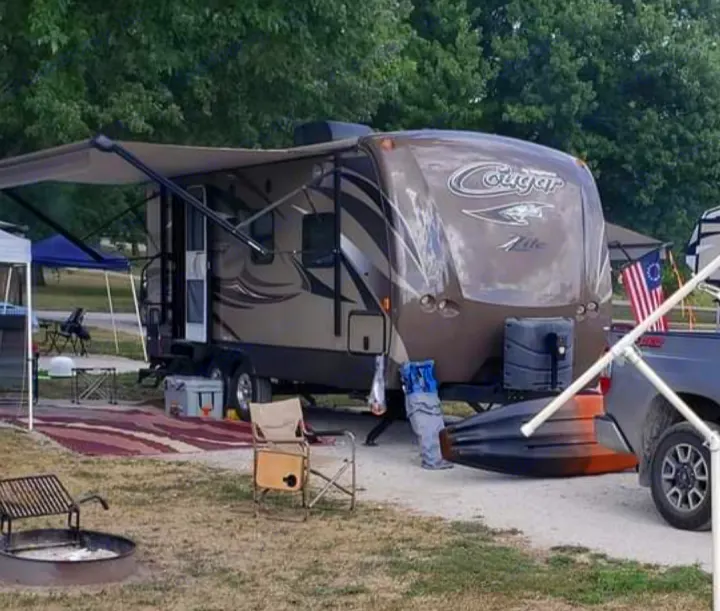 RV rental ready for adventure. A travel trailer parked at a wooded campsite with awning, fire pit, and kayak.. Keystone RV Cougar X-Lite 2015