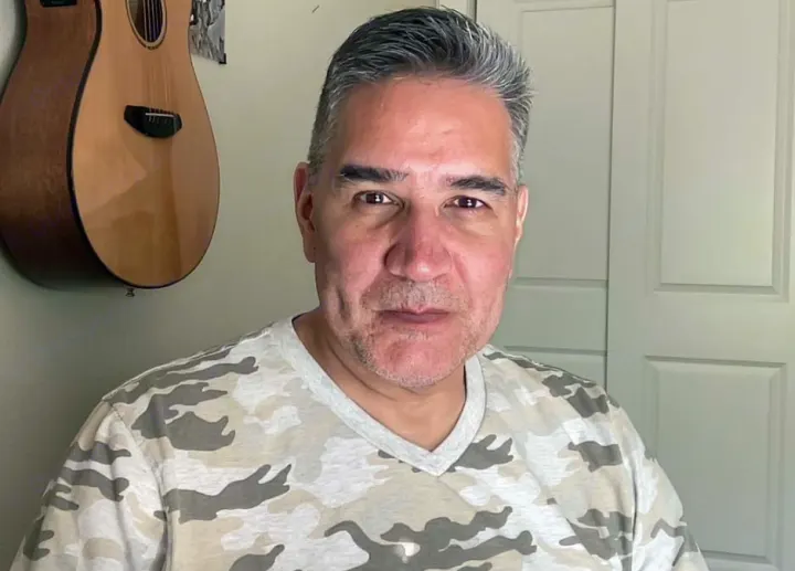 A man in a camo shirt looks directly at the camera, with a guitar behind him. Considering an RV rental adventure.. Little Guy Other 2012