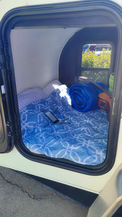 Cozy RV rental interior with a bed, blue bedding, phone, glasses, guitar, & rolled sleeping bag. Ready for adventure!. Little Guy Other 2012
