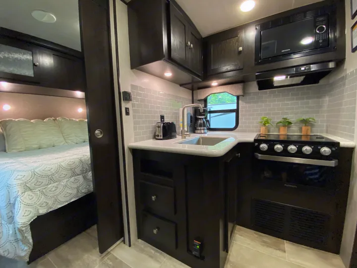 Modern RV rental interior with full kitchen, sink, stove, and a glimpse of the comfortable bedroom.. Heartland RVs North Trail 2019