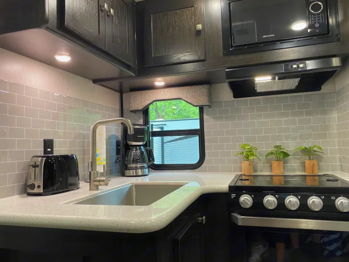 Bright RV rental kitchen with dark cabinets, gray subway tile backsplash, and essential modern appliances.. Heartland RVs North Trail 2019