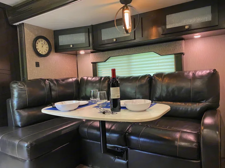 Cozy RV rental dining area featuring black leather U-shaped seating, a table set with wine and bowls, and overhead cabinets.. Heartland RVs North Trail 2019