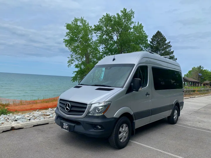 Explore with this silver Mercedes Sprinter **RV rental** campervan parked by the water under a cloudy sky.. Mercedes Benz 2017 Sprinter Van 2017