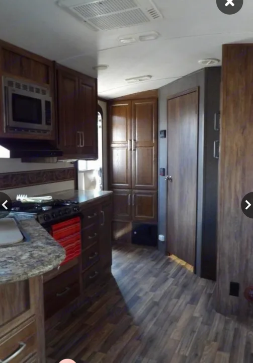 This RV rental showcases a compact kitchen with a stove, microwave, and ample wood cabinetry, leading to a hallway.. Keystone RV Cougar X-Lite 2015