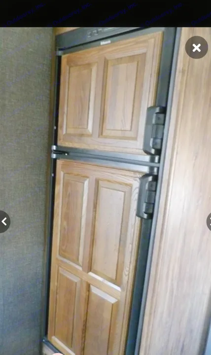 Wood-paneled two-door refrigerator, commonly found in an rv rental, blending with the RV's interior wood finishes.. Keystone RV Cougar X-Lite 2015