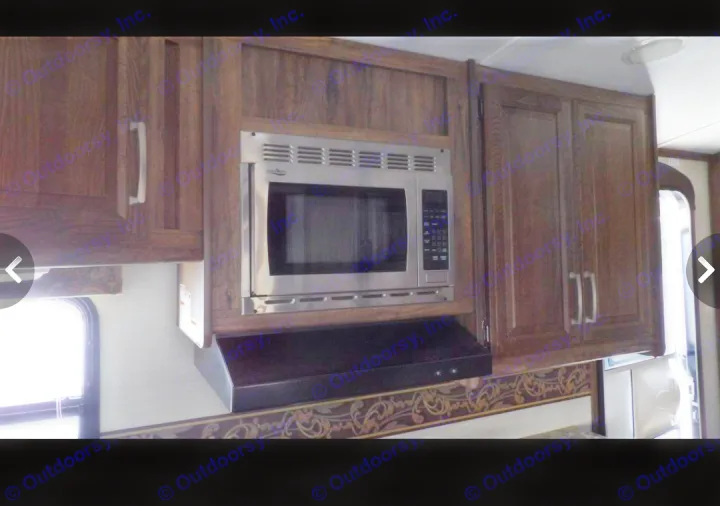 Well-equipped RV rental kitchen featuring a built-in microwave, range hood, and ample wooden cabinetry.. Keystone RV Cougar X-Lite 2015