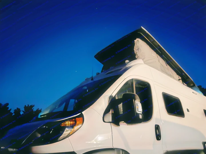 White RV rental camper van with pop-top extended, under a dark blue night sky with stars. Perfect for travel!. Winnebago Solis 2022