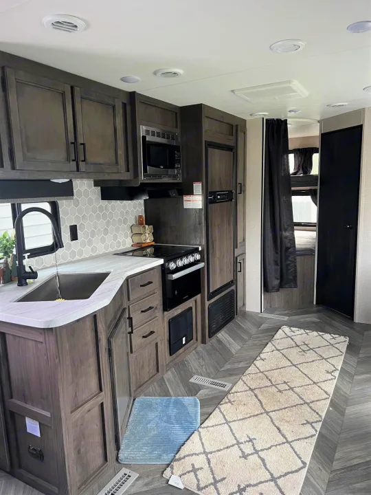 Explore this modern RV rental's well-appointed kitchen, featuring dark cabinets, white counters, and stylish flooring.. Highland Ridge Open Range Olympia 2022