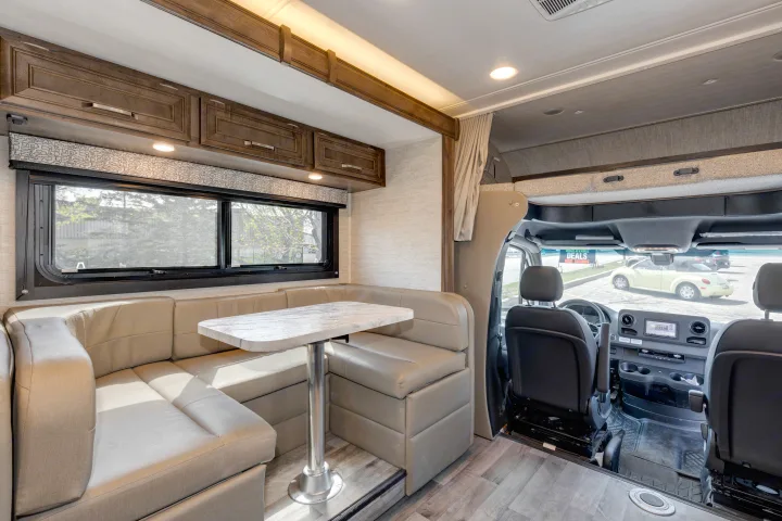 Spacious rv rental interior showing dining area, overhead cabinets, front cockpit, and cab-over bunk.. Jayco Melbourne 2022