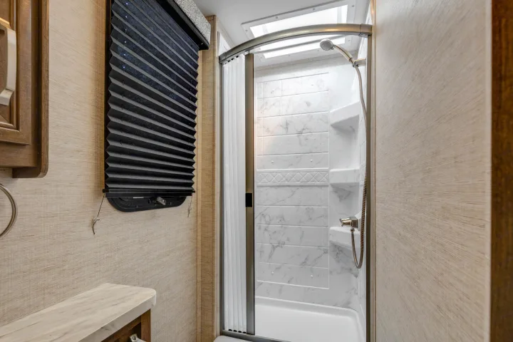 Inside an RV rental: a modern, compact bathroom with a bright shower, marbled walls, and a pleated window blind.. Jayco Melbourne 2022