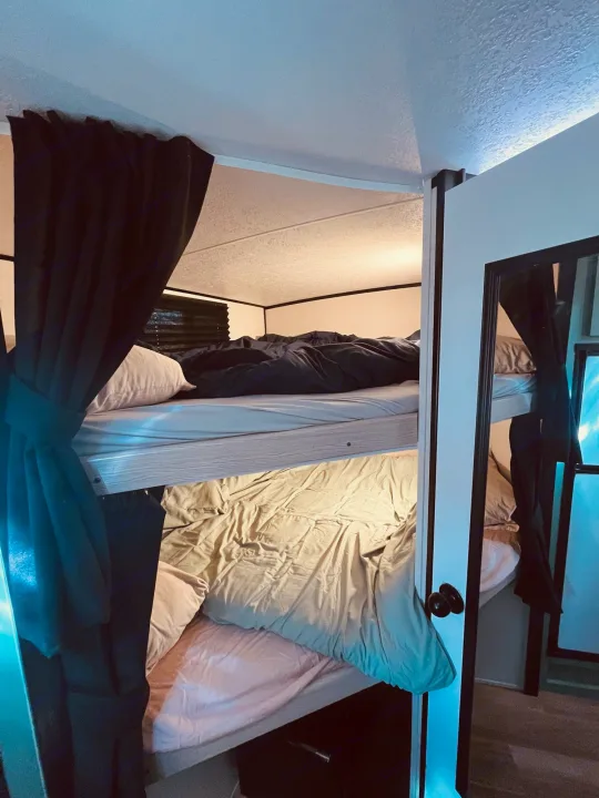 Inside an RV rental: two compact bunk beds with bedding. Curtains and a mirror enhance the cozy sleeping area.. Forest River Coachmen Apex Nano Off-Grid 2022