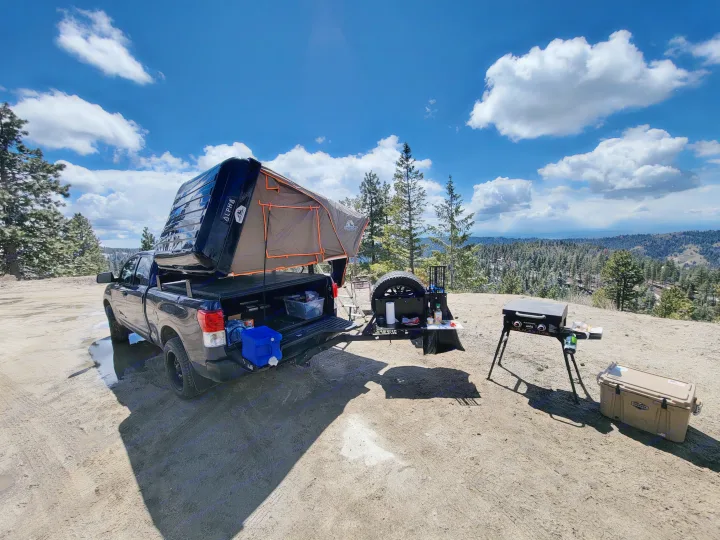 Truck with rooftop tent, grill, & cooler set up for camping in scenic mountains. An ideal RV rental alternative for adventure.. Toyota Tundra 2011
