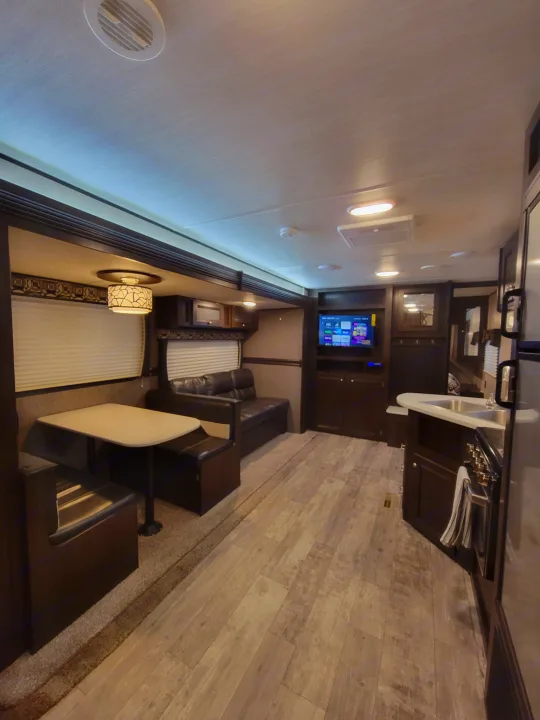 Spacious RV rental interior: dining booth, lounge with TV, and equipped kitchen. Perfect for your next adventure.. Heartland RVs Pioneer 2019