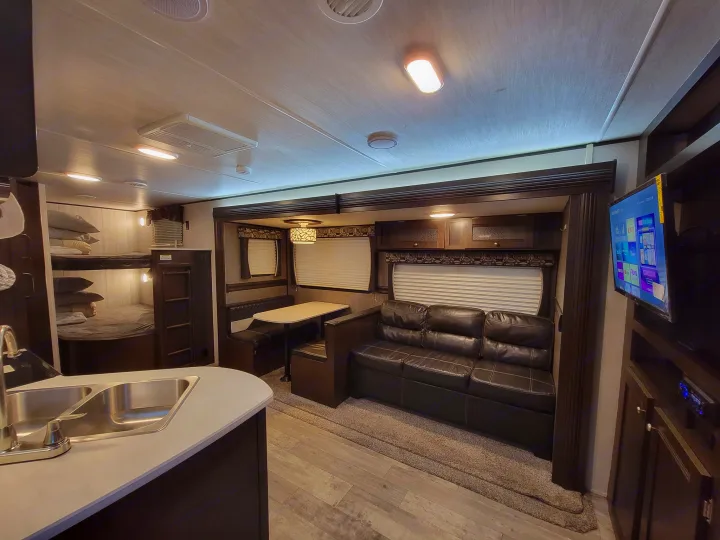 This spacious RV rental interior features a kitchen, dinette, bunk beds, and sofa, perfect for family adventures.. Heartland RVs Pioneer 2019