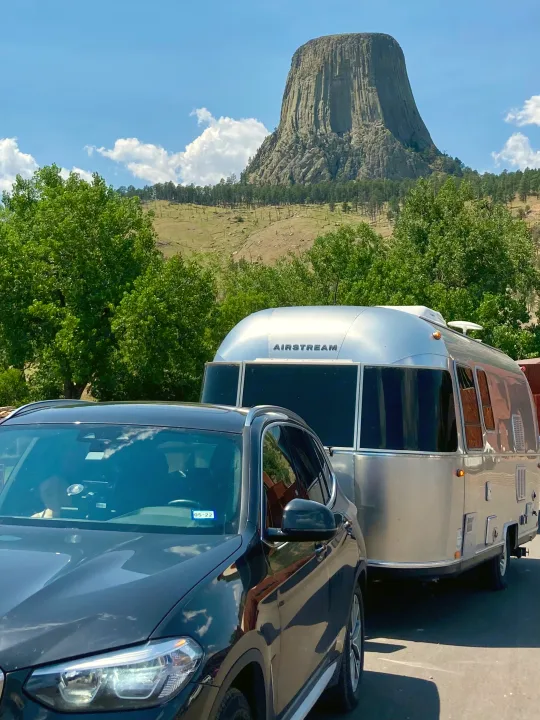 Devil's Tower frames a silver Airstream trailer and black SUV, showcasing RV rental adventures in nature.. Airstream Sport 2019