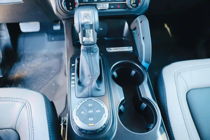 RV rental's rugged interior: Automatic shifter with Bronco emblem, G.O.A.T. modes 4x4 dial, and cup holders ready for adventure.. Ford Bronco 2024