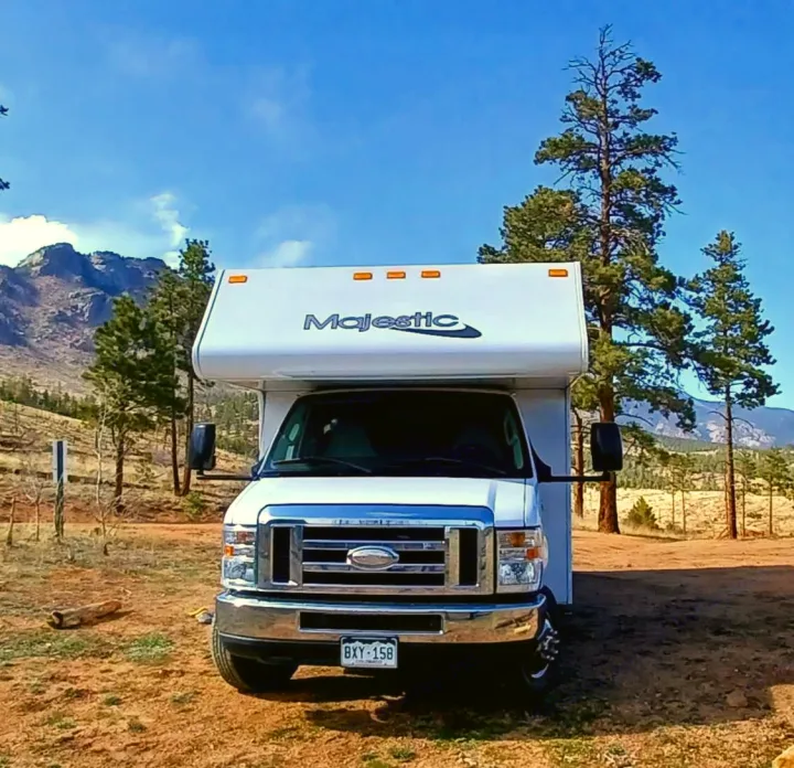 Majestic rv rental parked in a scenic mountain setting with pine trees under a clear blue sky, ideal for nature travel.. Thor Majestic 2015