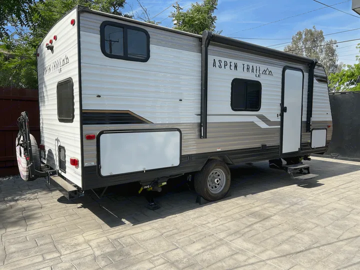An Aspen Trail LE travel trailer, ideal for rv rental, is parked on textured pavers. A leisure vehicle in a residential setting.. Dutchmen Other 2021