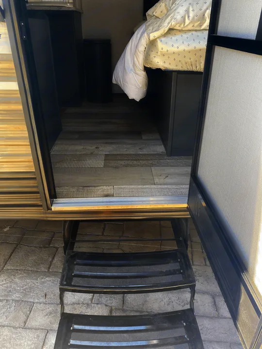 Open door of an RV rental revealing its interior, including steps, wood flooring, and bedroom area.. Dutchmen Other 2021