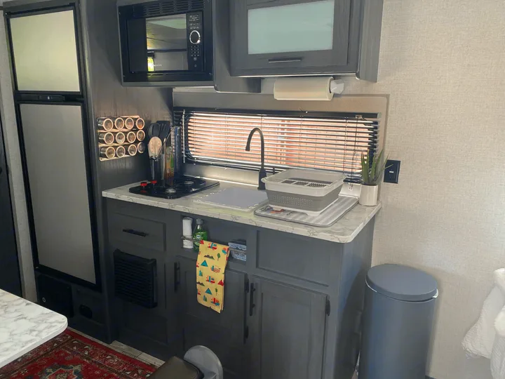 Modern RV rental kitchen with fridge, microwave, sink, and stovetop. Features dark grey cabinets and light countertops.. Dutchmen Other 2021