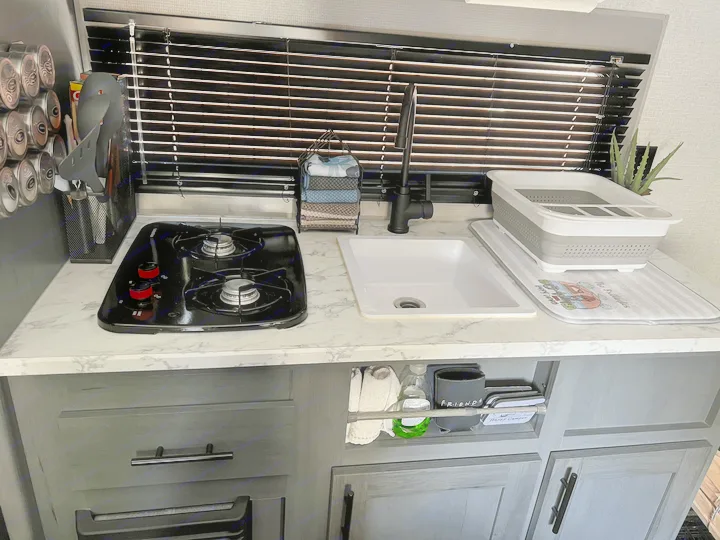 A compact RV rental kitchen featuring a two-burner stove, sink, and stylish storage solutions.. Dutchmen Other 2021